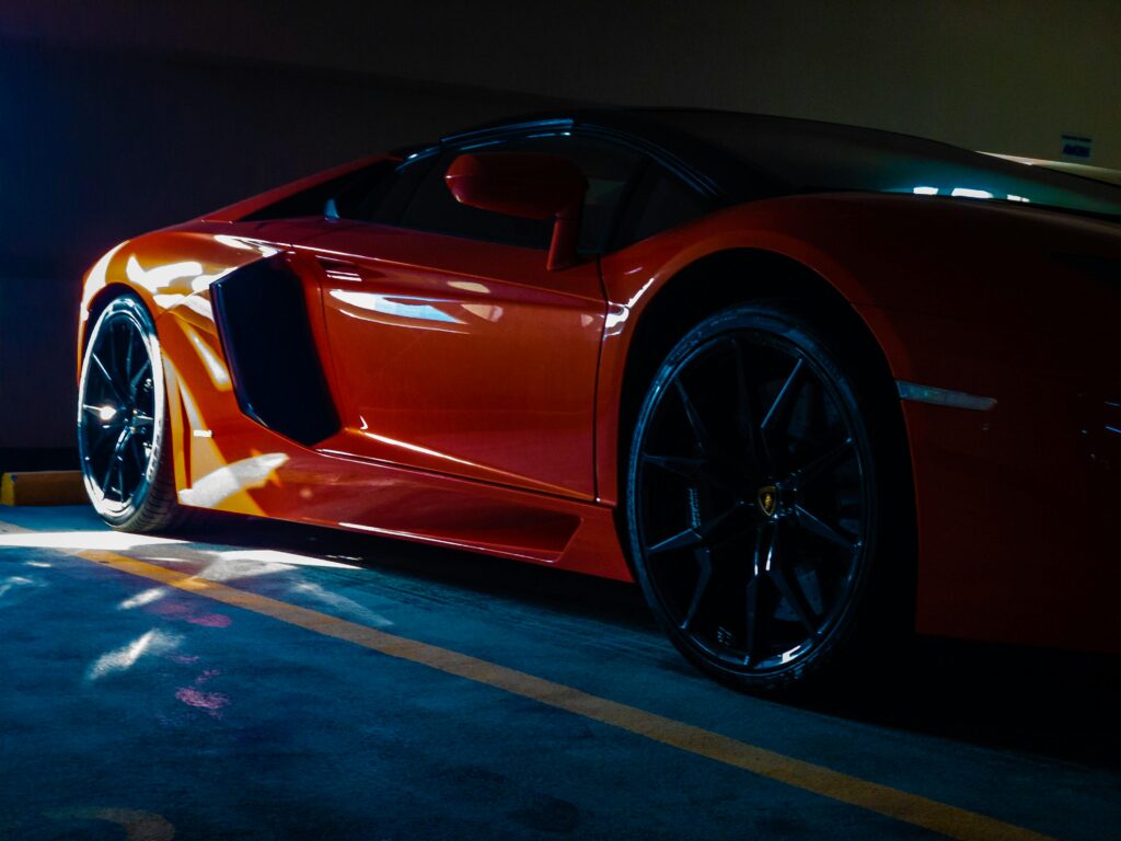 pexels-photo-2631489-2631489 Close-up of a vibrant orange sports car parked in a sunlit garage, showcasing luxury and modern design.